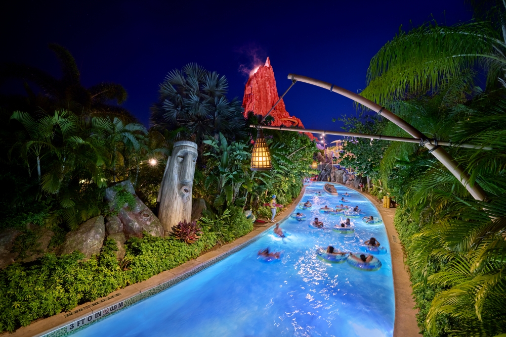 A group of people floating down a lazy river at night with a glowing volcano in the distance at Volcano Bay Nights.