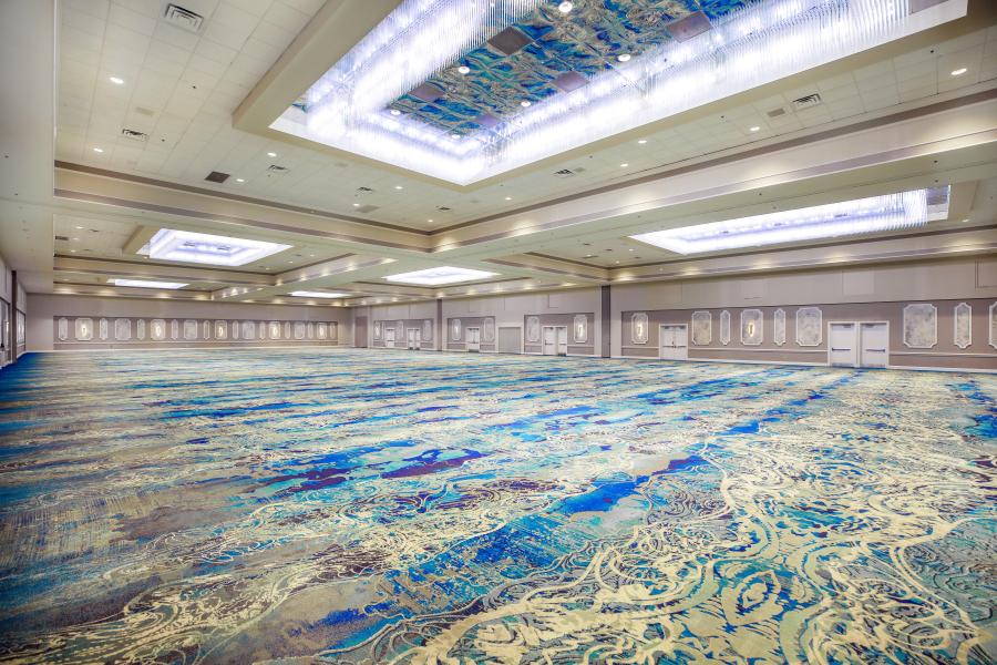 A large ballroom with grand rectangular light fixtures, a blue carpet, and plenty of lighting around the perimeter of the room.