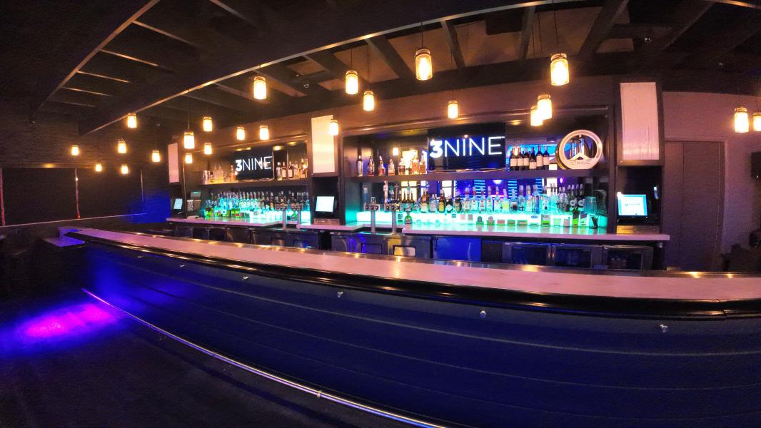 A dimly lit bar with a sign reading 3NINE and LED backlights behind bottles. 