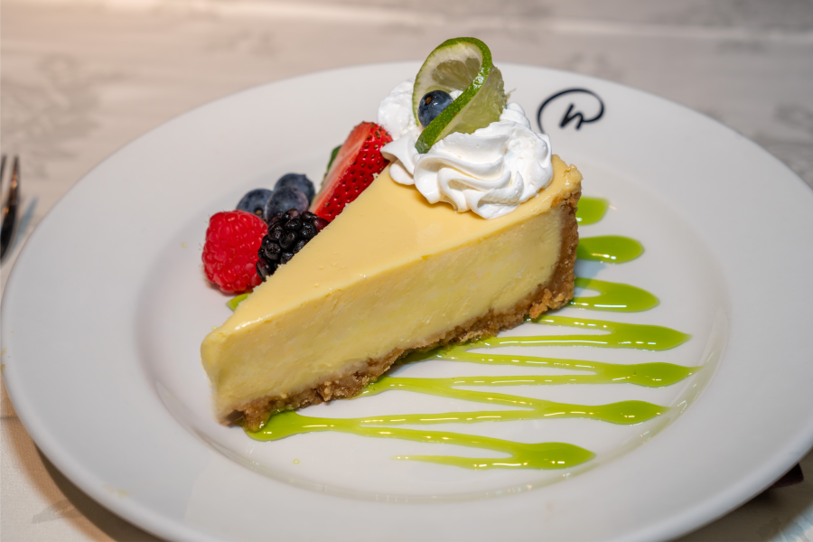 A slice of key lime pie on a plate, with a drizzle of green key lime sauce and garnished with fresh berries and whipped cream.