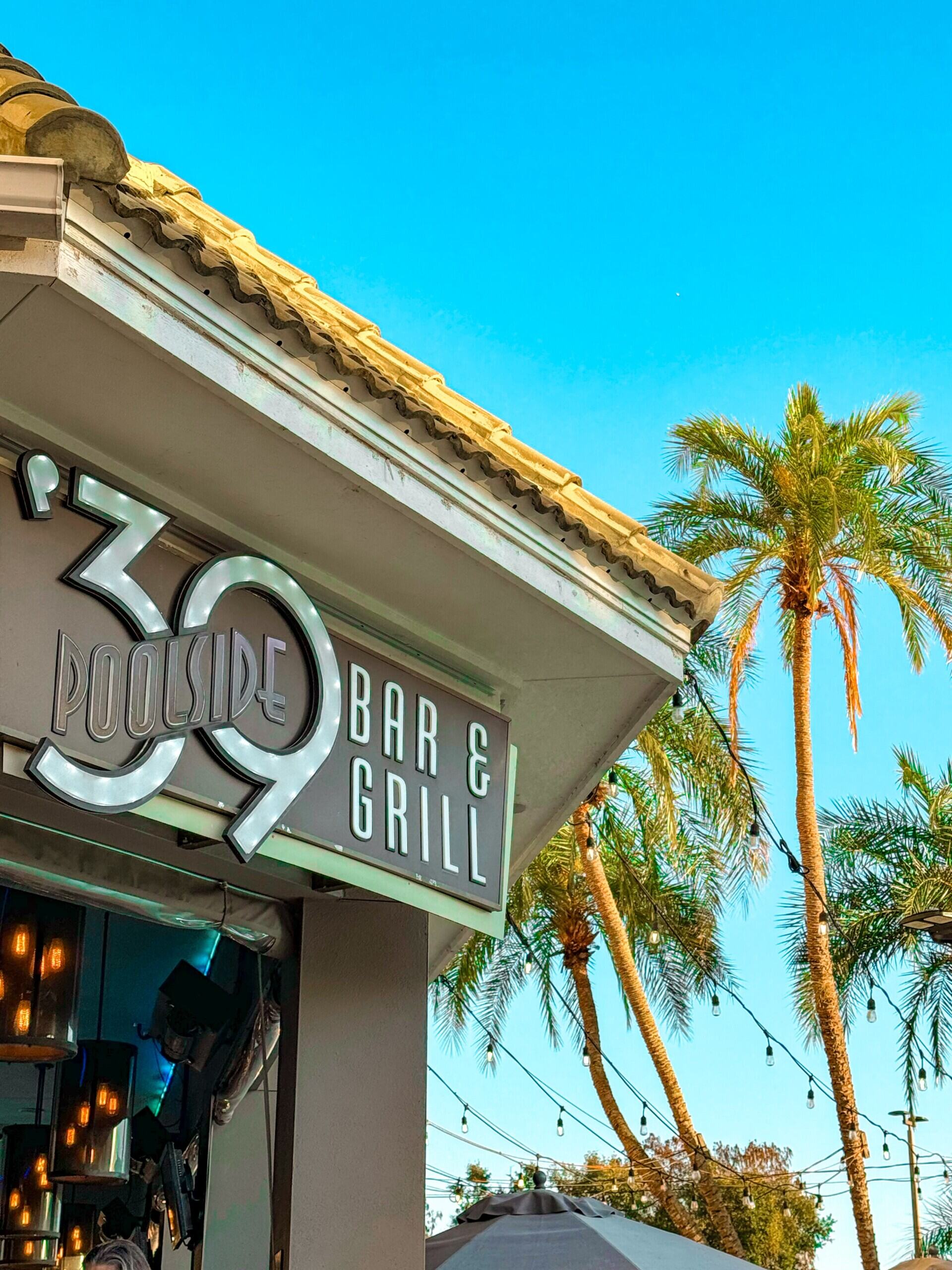 A close-up of the sign for 39 Poolside Bar and Grill on the outside of a restaurant, with palm trees in the background.