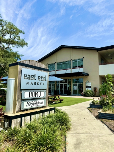 A two-story building with a green grassy area and outdoor seating behind a large sign reading East End Market and DOMU.