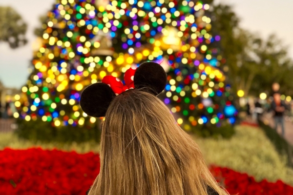 A woman wearing Minnie Mouse ears faces away from the camera toward a large glittering Christmas tree while visiting EPCOT, one of many things to do on Thanksgiving.