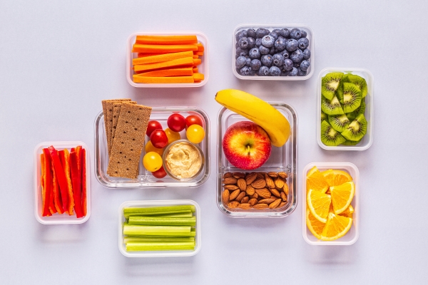 An organized display of containers with cut fruits, vegetables, nuts, and other healthy snacks.