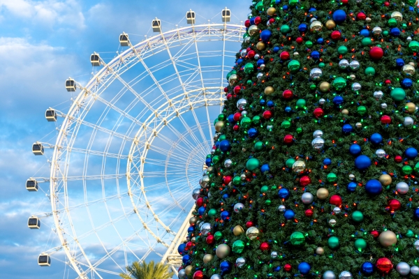 The large Orlando Eye observation wheel peeks out against a blue sky from behind a decorated Christmas tree in the foreground.