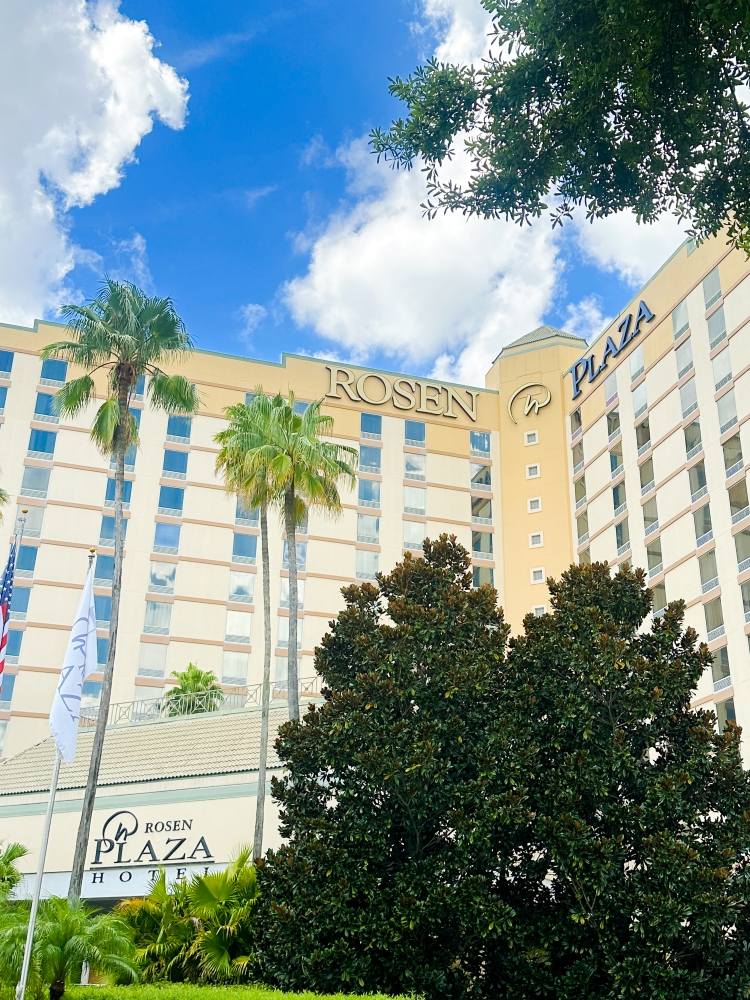 An exterior shot of Rosen Plaza, a destination for bleisure in Orlando, surrounded by leafy trees and palm trees.