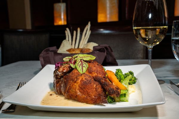 A crispy rotisserie chicken on a plate garnished with brightly colored vegetables for Magical Dining at Jack's Place.