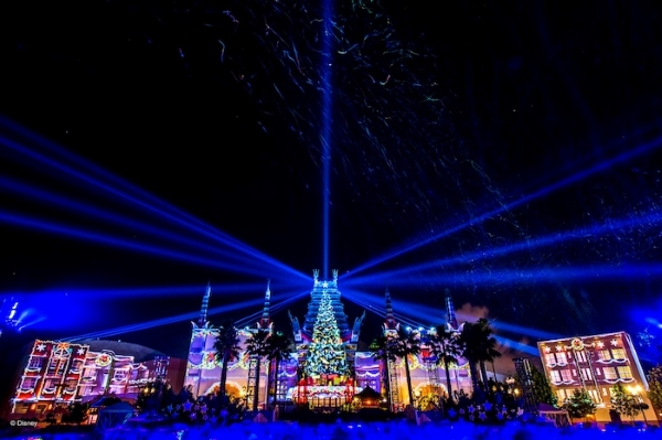 Hollywood Studios at night with a large projection show and blue lasers blasting into the sky.