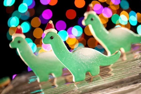 Three dinosaur cookies with Santa hats against a twinkling backdrop.