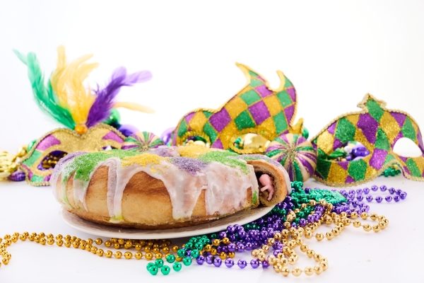 An iced king cake surrounded by colorful beads, masks, and other Mardi Gras paraphernalia. 