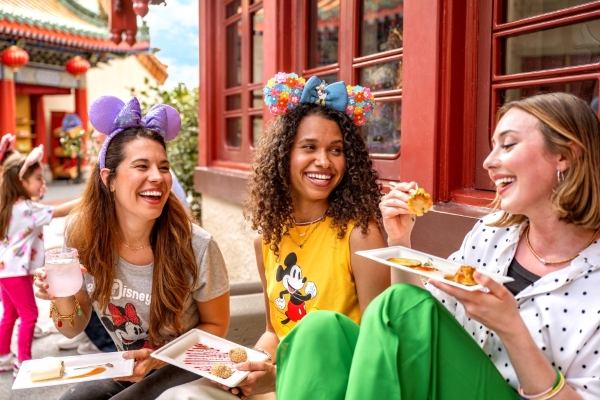 Three women wearing Minnie Mouse ears sit outside and eat. 