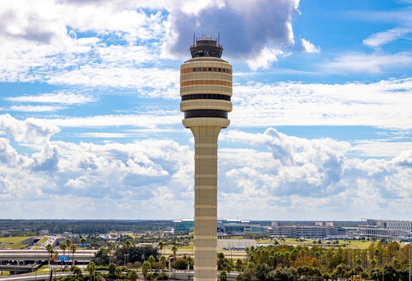 The tall air traffic control tower at Orlando International Airport (MCO) against a blue cloudy sky.