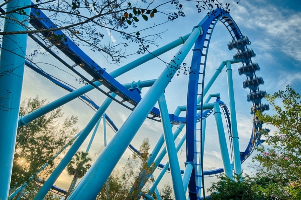 An upward view of a large blue roller coaster track against a twilight sky.