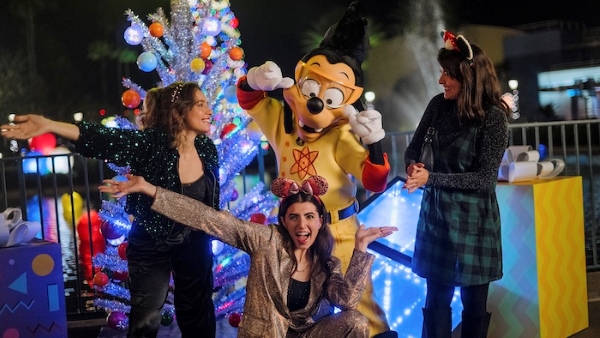 Three women pose with Max Goof dressed as Powerline in front of a decorated silver Christmas tree.