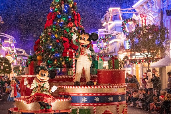 Mickey and Minnie in holiday attire on a grand float with a Christmas tree gliding down Main St. USA.