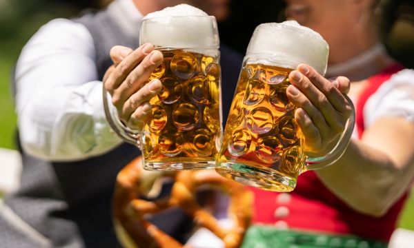 A close-up of a man and woman clinking together two full steins of beer at an Oktoberfest celebration.