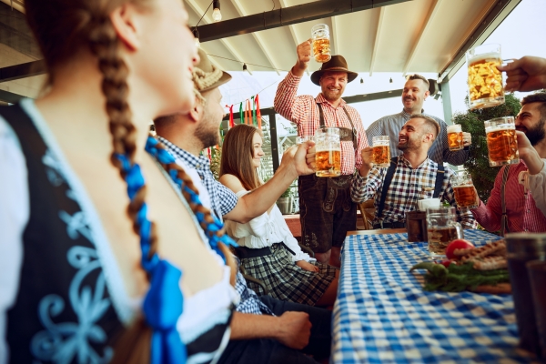 A group of people in Bavarian clothing sit around a table raising steins of beer during Oktoberfest.