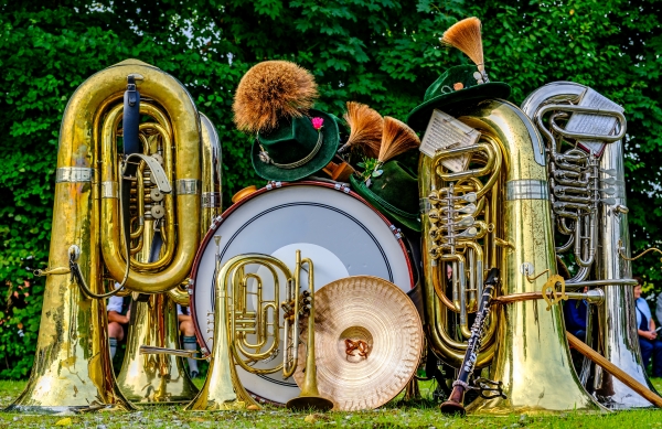 An assortment of shiny brass instruments and Bavarian green hats sits on the lawn of an Oktoberfest celebration.