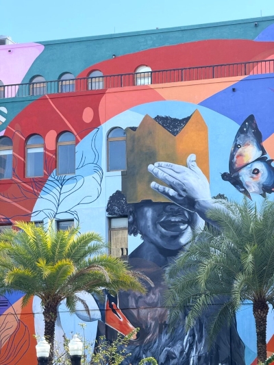 A colorful mural of a child covering their eyes with a golden crown, one example of art in Orlando.