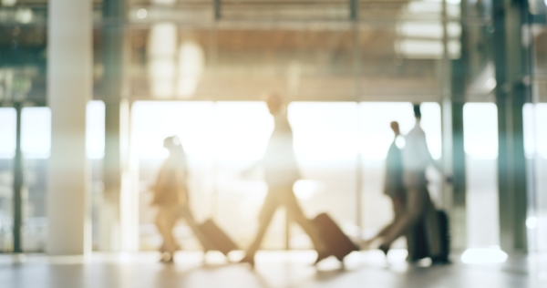 An out-of-focus shot of travelers walking through an airport with suitcases.