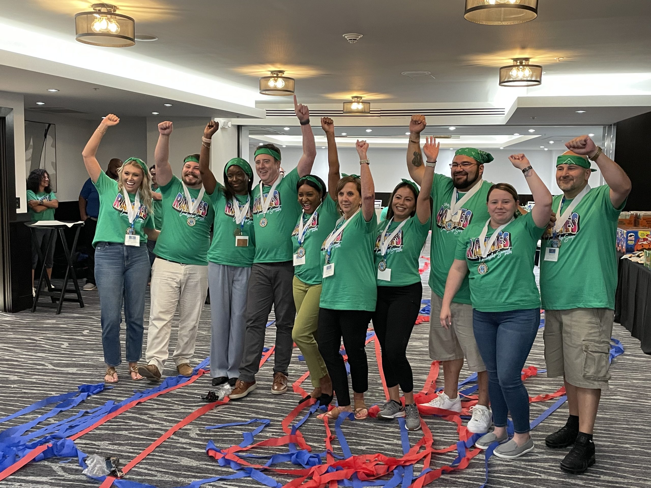 A group of adults in matching green t-shirts wearing medals and cheering. 