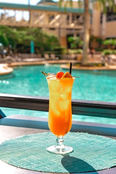 A tall orange tropical cocktail in a hurricane glass sits on a table beside the pool at Rosen Plaza in Orlando.