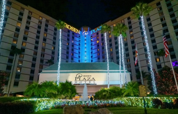 The front entrance of Rosen Plaza at night, with palm trees and landscaping wrapped in Christmas lights. 