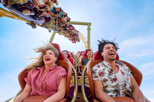 A man and woman at the front of a roller coaster car screaming as a second car glides overhead.