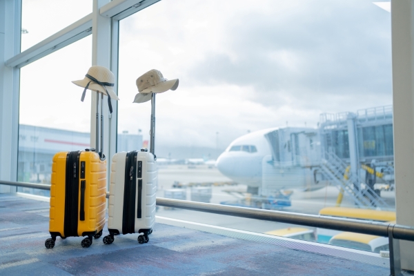 Hats rest atop two suitcases in front of a large airport window.