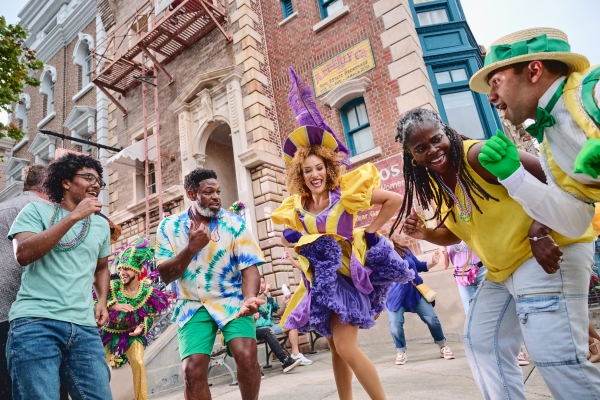 A group of people in Mardi Gras beads and costumes dance in the street at Universal Orlando.