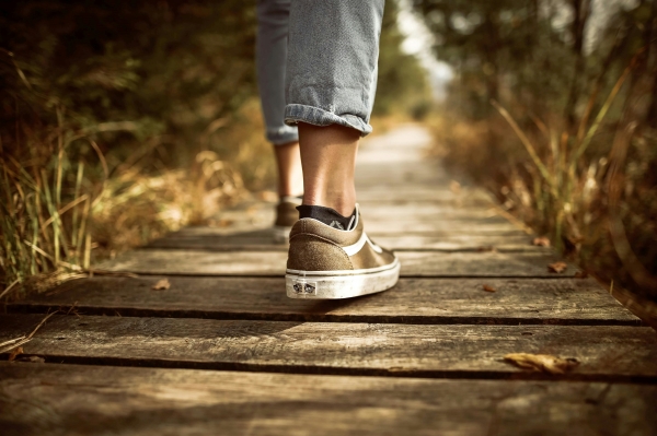 A close-up of the back of a pair of shoes walking along a boardwalk.
