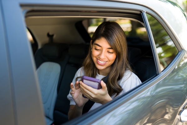 A woman in the backseat of a rideshare in Orlando looks at her phone while smiling.
