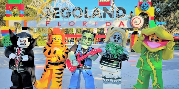 Five LEGO characters in Halloween costumes stand in front of the LEGOLAND Florida sign.