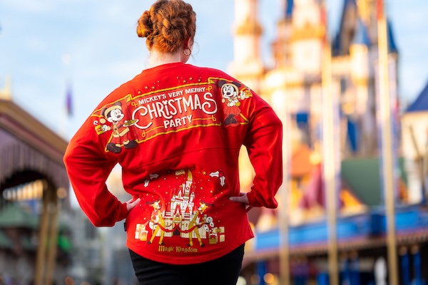 A woman wearing a festive red spirit jersey faces away from the camera, looking at Cinderella Castle.