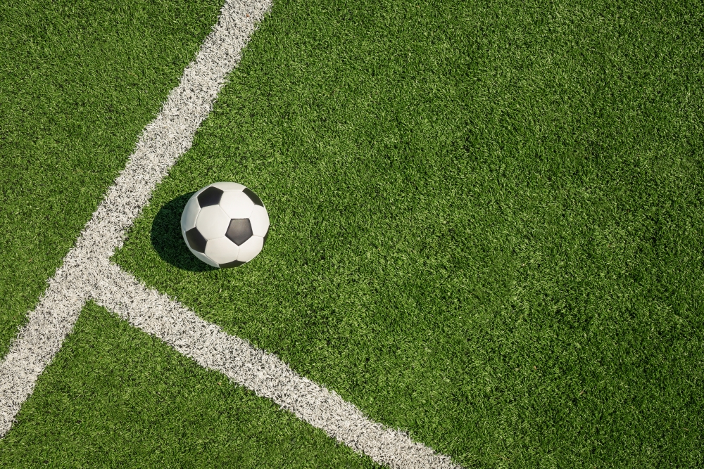 An overhead shot of a soccer ball on turf beside white boundary lines.