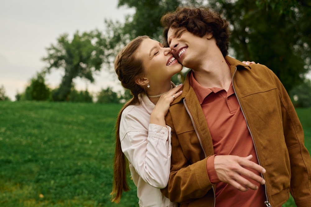 A young woman rests on the shoulder of a young man outdoors, romantically embracing for national girlfriend's day